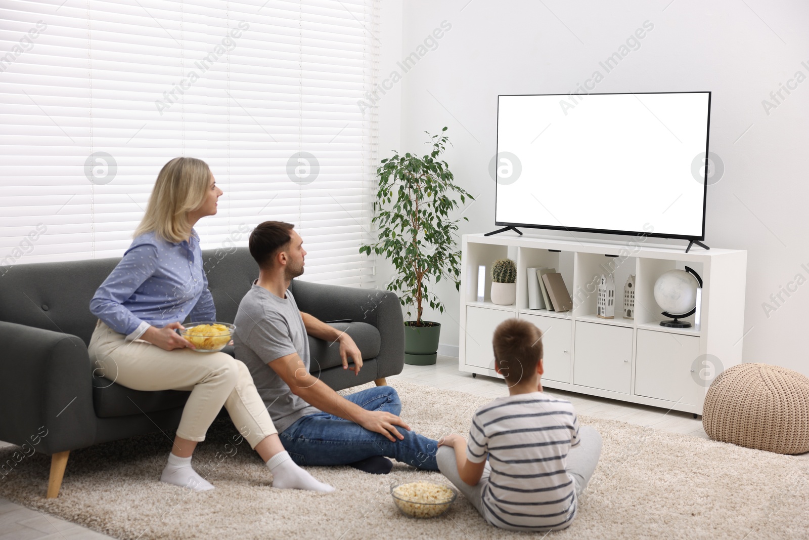 Photo of Happy family with snacks watching tv together at home