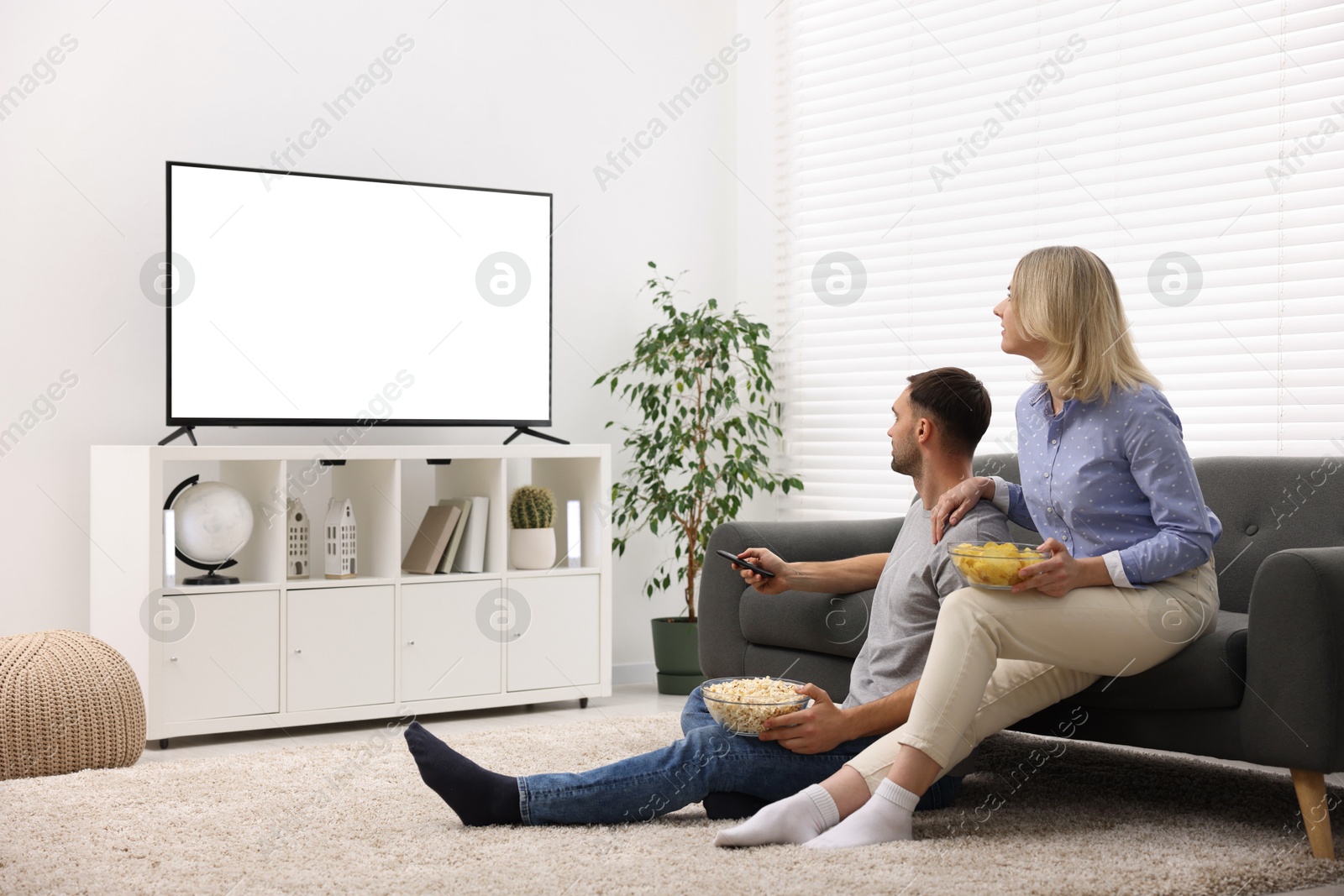 Photo of Lovely couple with snacks watching tv at home