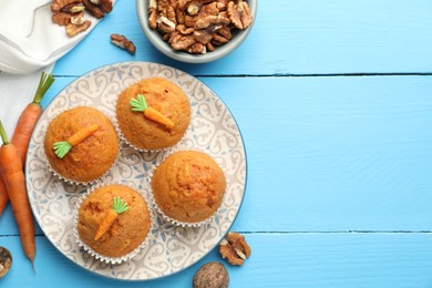 Photo of Tasty carrot muffins, walnuts and fresh vegetables on light blue wooden table, flat lay. Space for text