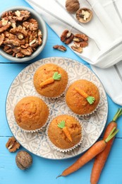 Photo of Tasty carrot muffins, walnuts and fresh vegetables on light blue wooden table, flat lay