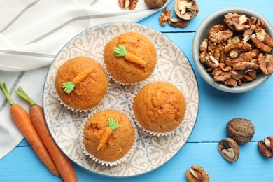 Photo of Tasty carrot muffins, walnuts and fresh vegetables on light blue wooden table, flat lay