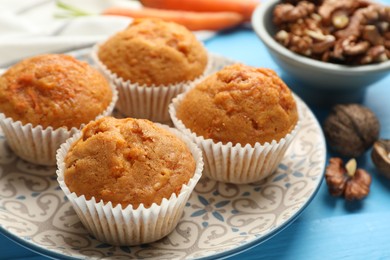 Photo of Tasty carrot muffins and walnuts on light blue wooden table, closeup