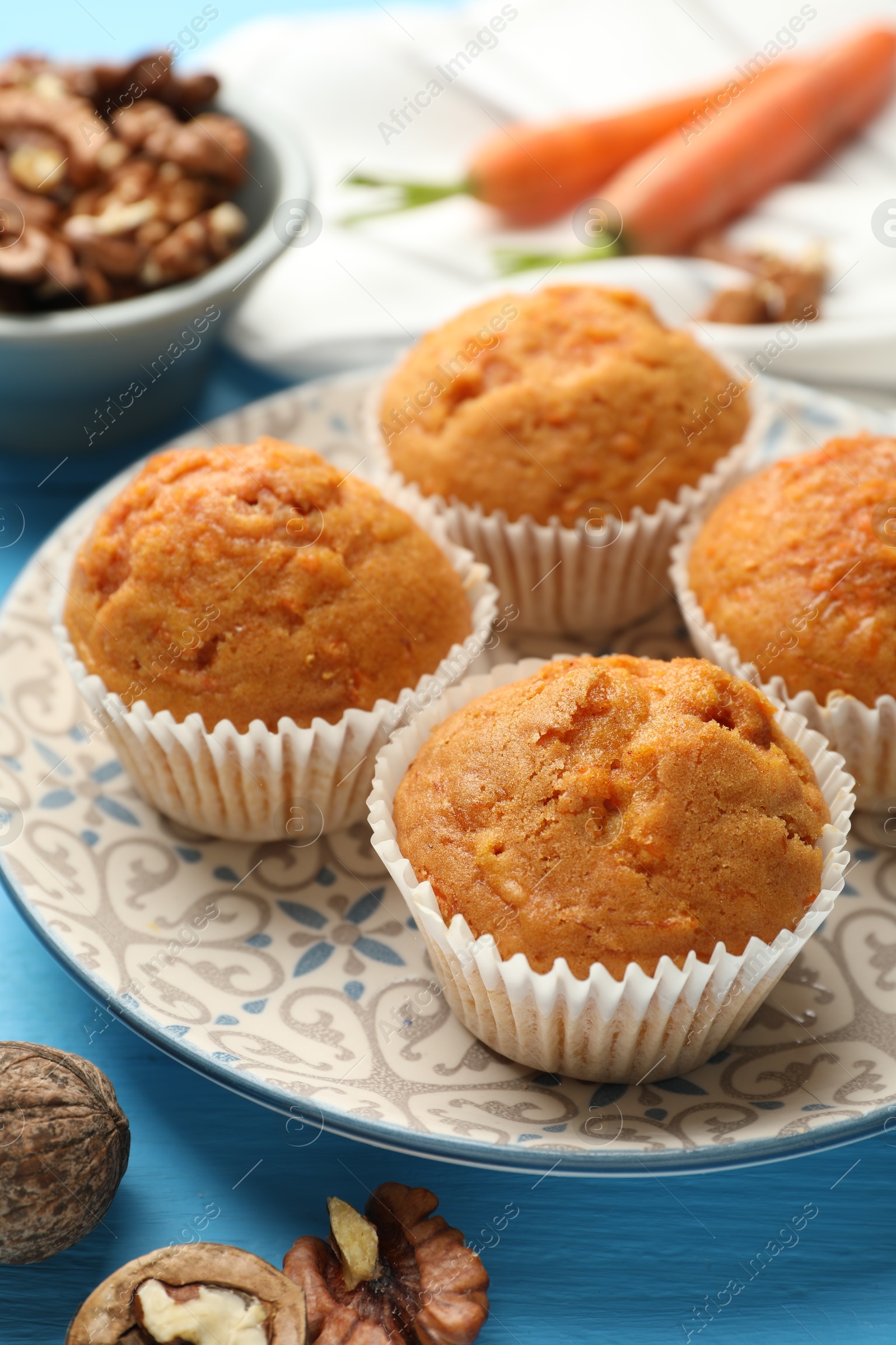 Photo of Tasty carrot muffins and walnuts on light blue wooden table, closeup