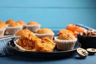 Photo of Tasty carrot muffins and walnuts on blue wooden table, closeup