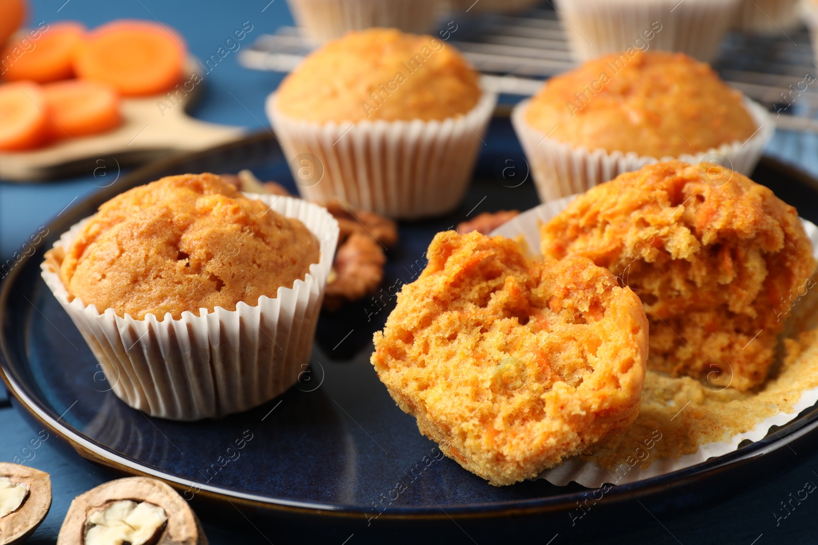 Photo of Tasty carrot muffins and walnuts on blue wooden table, closeup