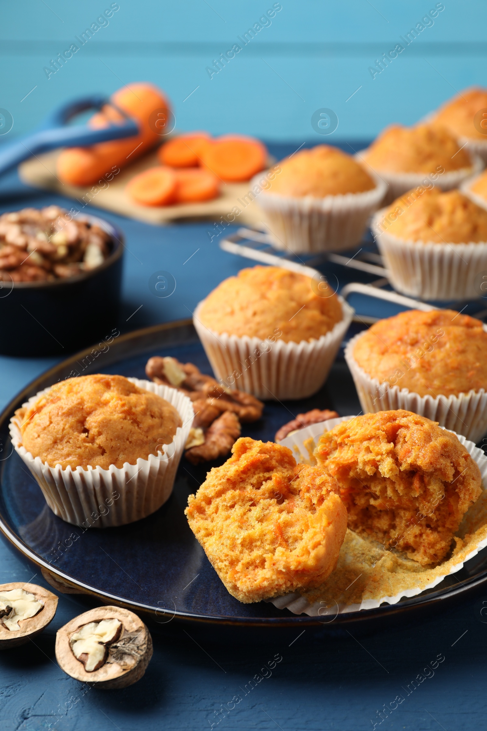 Photo of Tasty carrot muffins and walnuts on blue wooden table, closeup