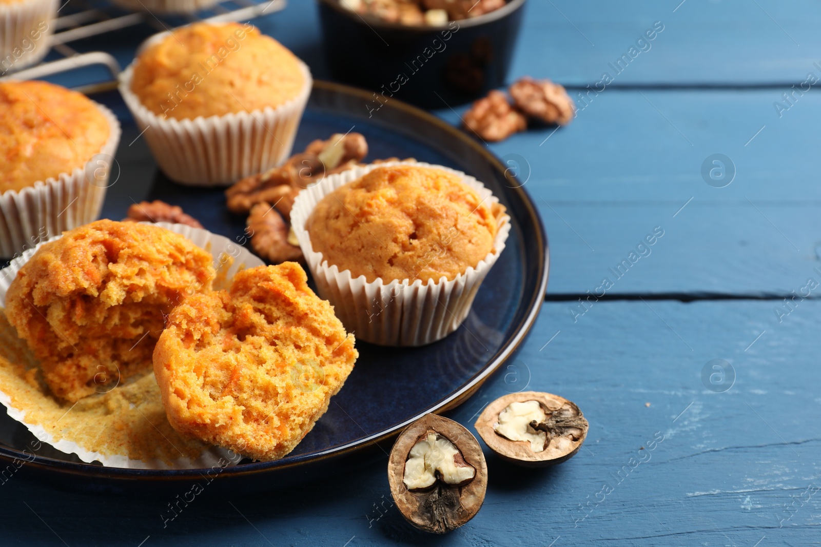 Photo of Tasty carrot muffins and walnuts on blue wooden table, closeup. Space for text