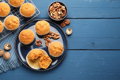 Photo of Tasty carrot muffins and walnuts on blue wooden table, flat lay. Space for text