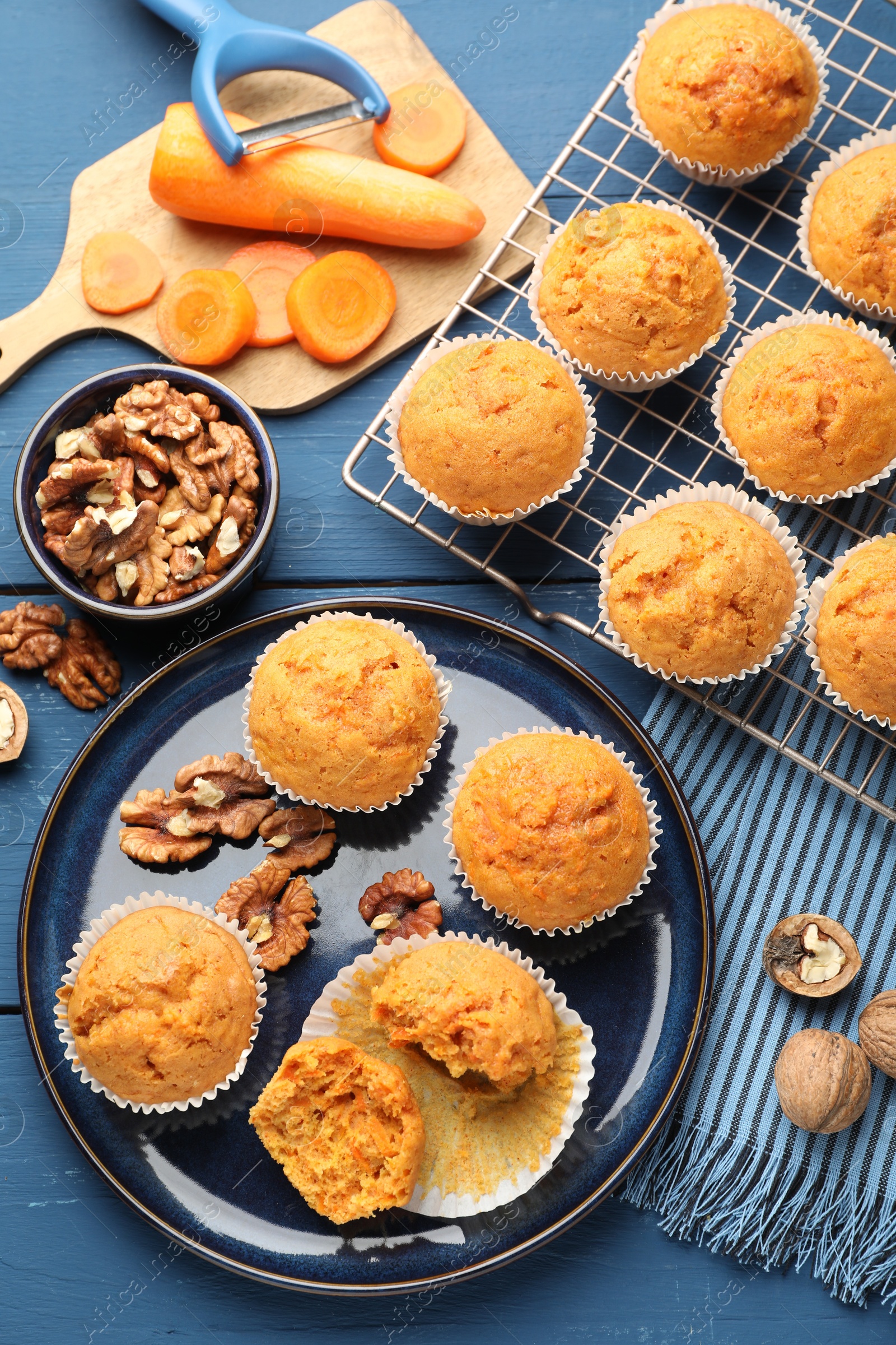 Photo of Tasty carrot muffins, walnuts and fresh vegetables on blue wooden table, flat lay