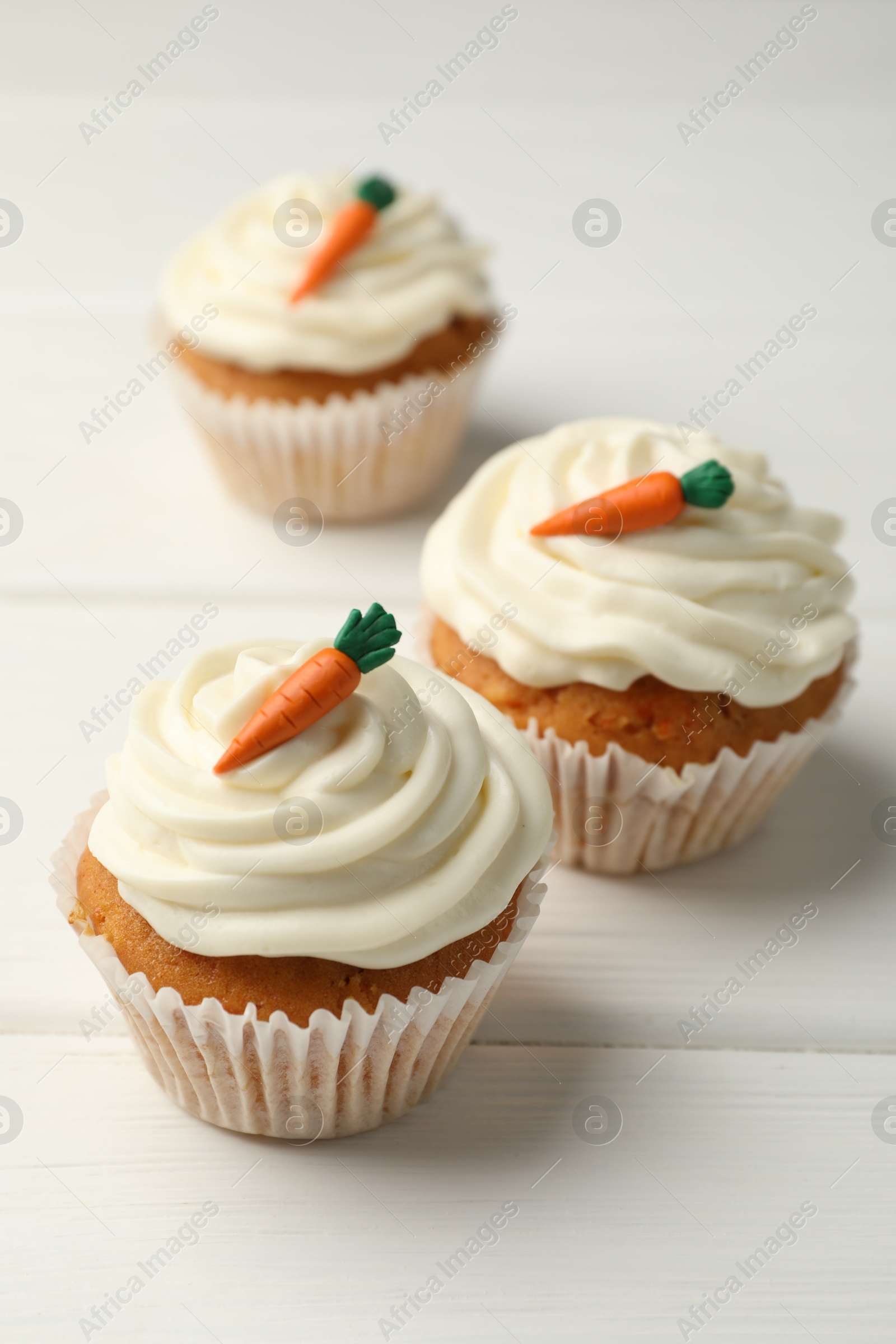 Photo of Tasty carrot muffins with cream on white wooden table, closeup