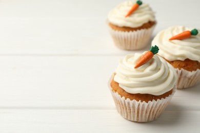 Photo of Tasty carrot muffins with cream on white wooden table, closeup. Space for text