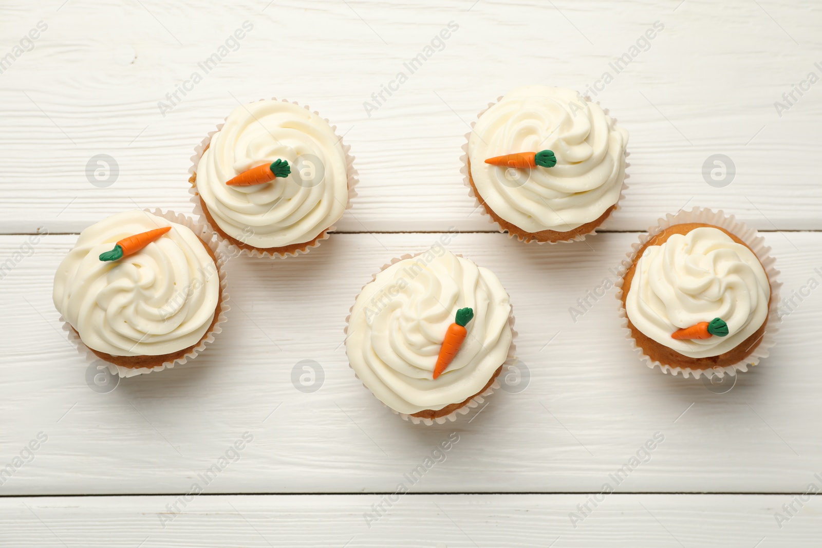 Photo of Tasty carrot muffins with cream on white wooden table, flat lay