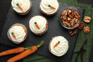 Photo of Tasty carrot muffins with cream, walnuts and fresh vegetables on black wooden table, flat lay