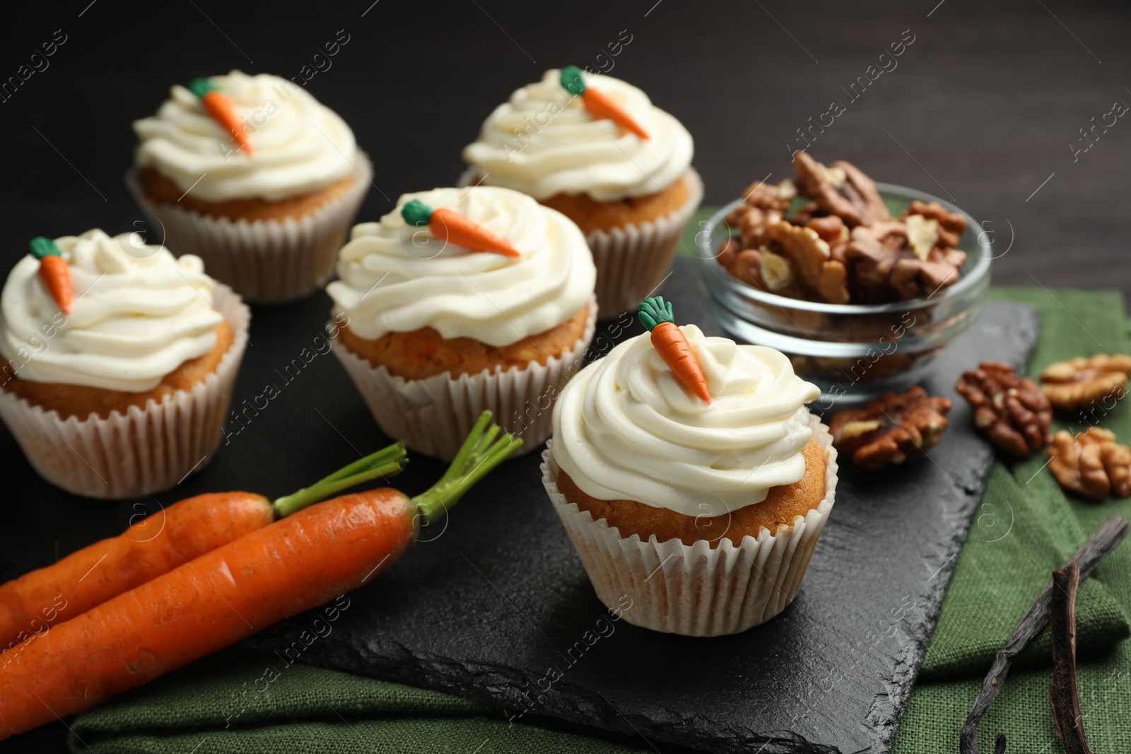 Photo of Tasty carrot muffins with cream, walnuts and fresh vegetables on black wooden table, closeup