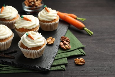 Photo of Tasty carrot muffins with cream, walnuts and fresh vegetables on black wooden table, closeup. Space for text