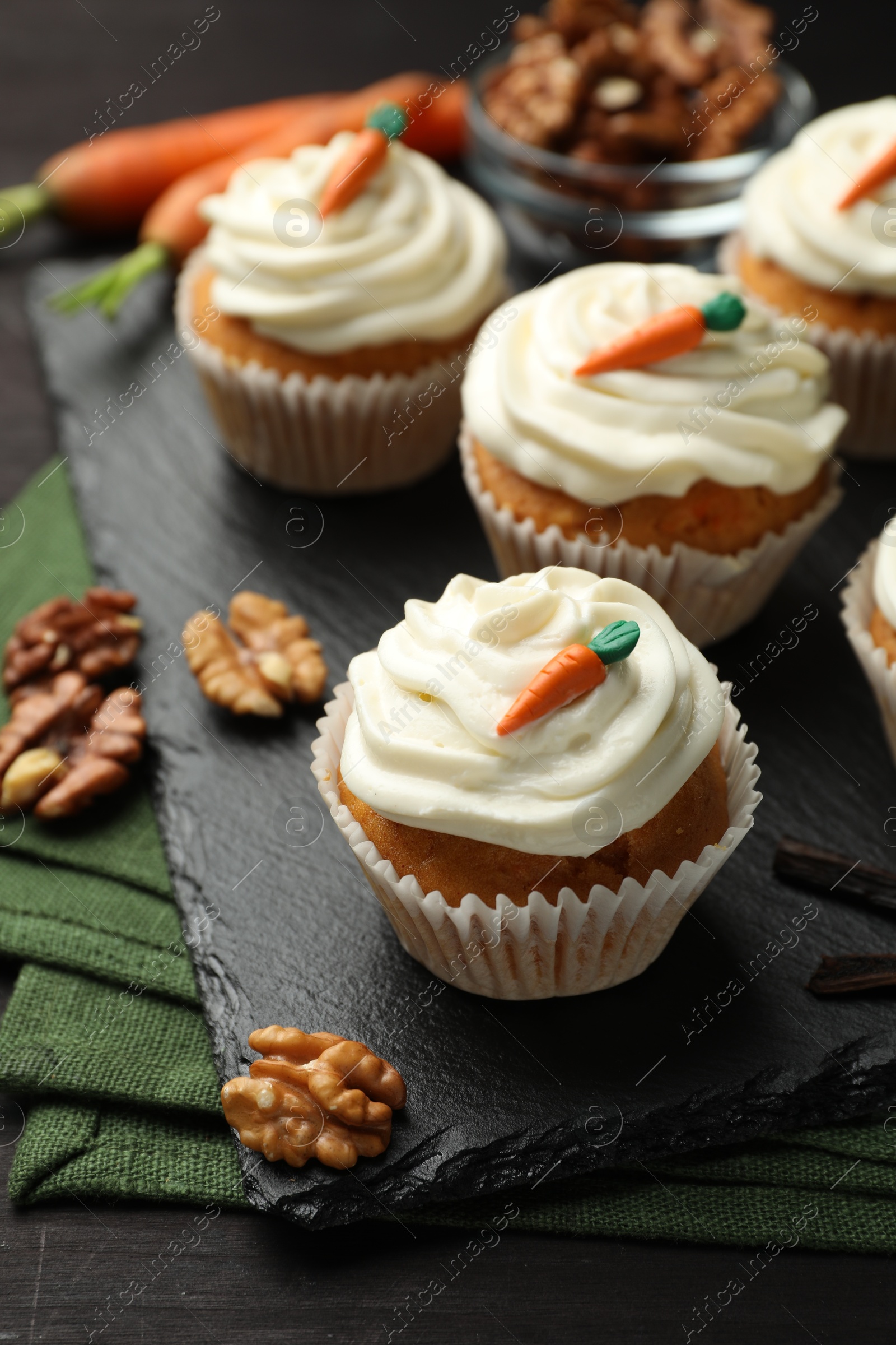 Photo of Tasty carrot muffins with cream and walnuts on black wooden table, closeup