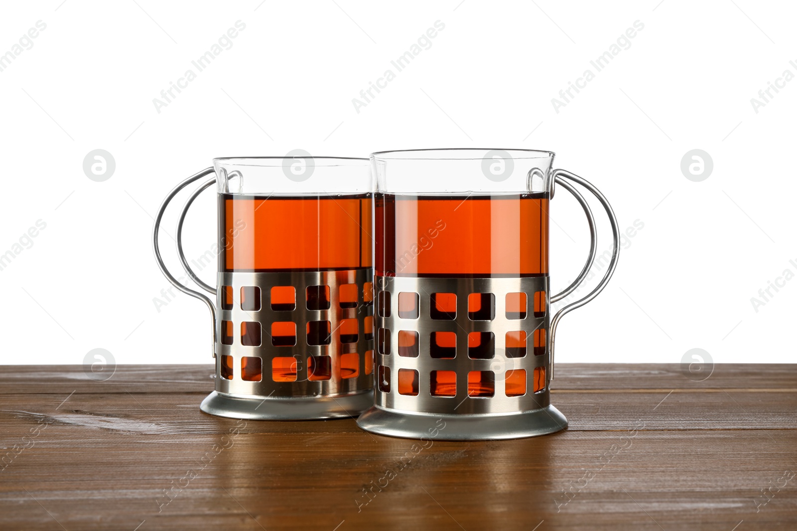 Photo of Glasses of aromatic tea in holders on wooden table against white background