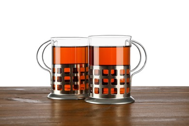 Glasses of aromatic tea in holders on wooden table against white background