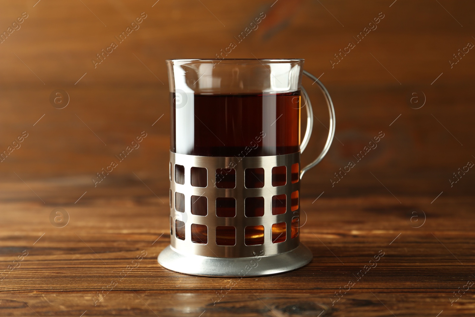 Photo of Glass of aromatic tea in holder on wooden table