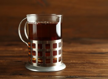 Photo of Glass of aromatic tea in holder on wooden table, space for text