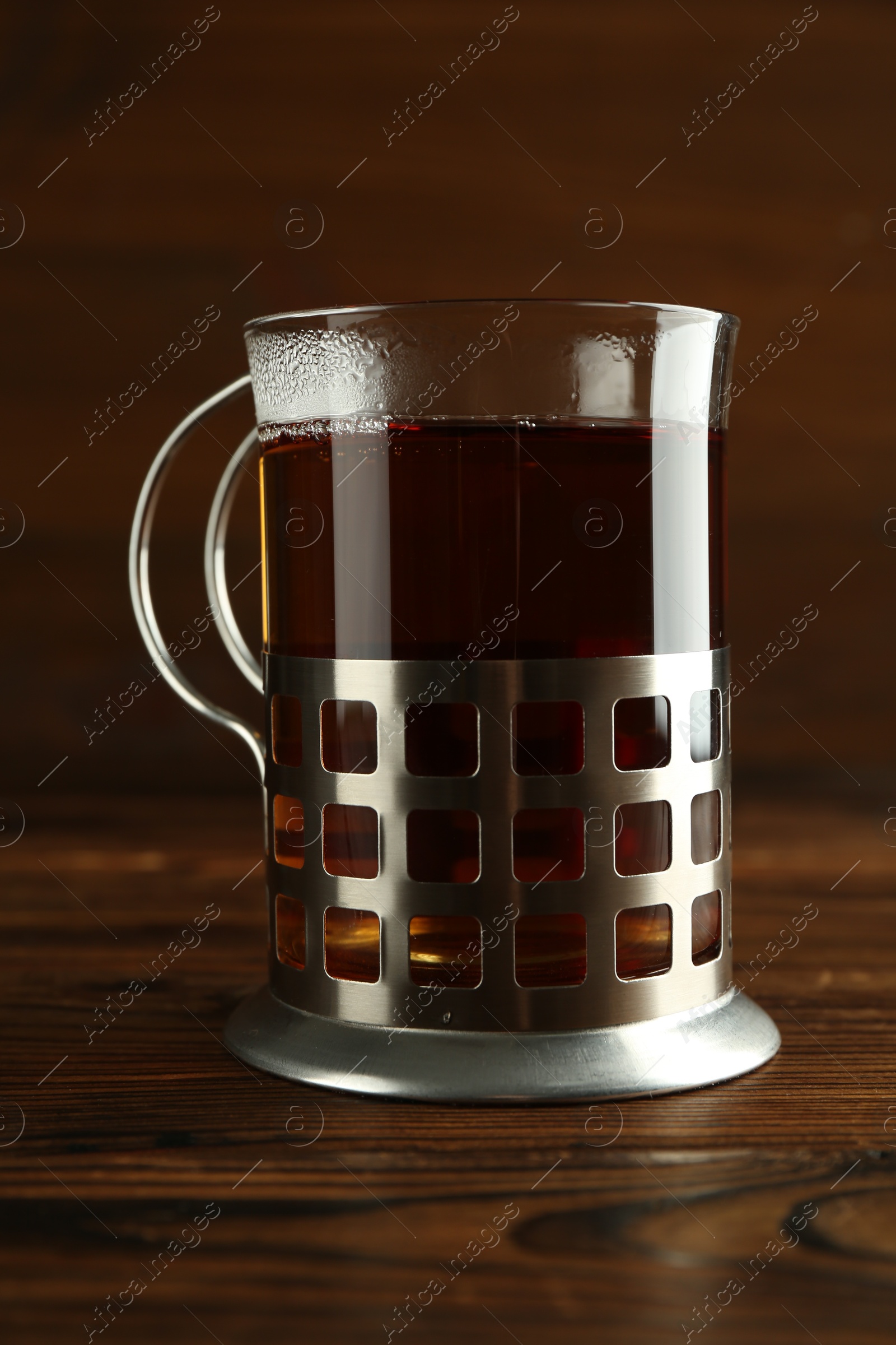 Photo of Glass of aromatic tea in holder on wooden table