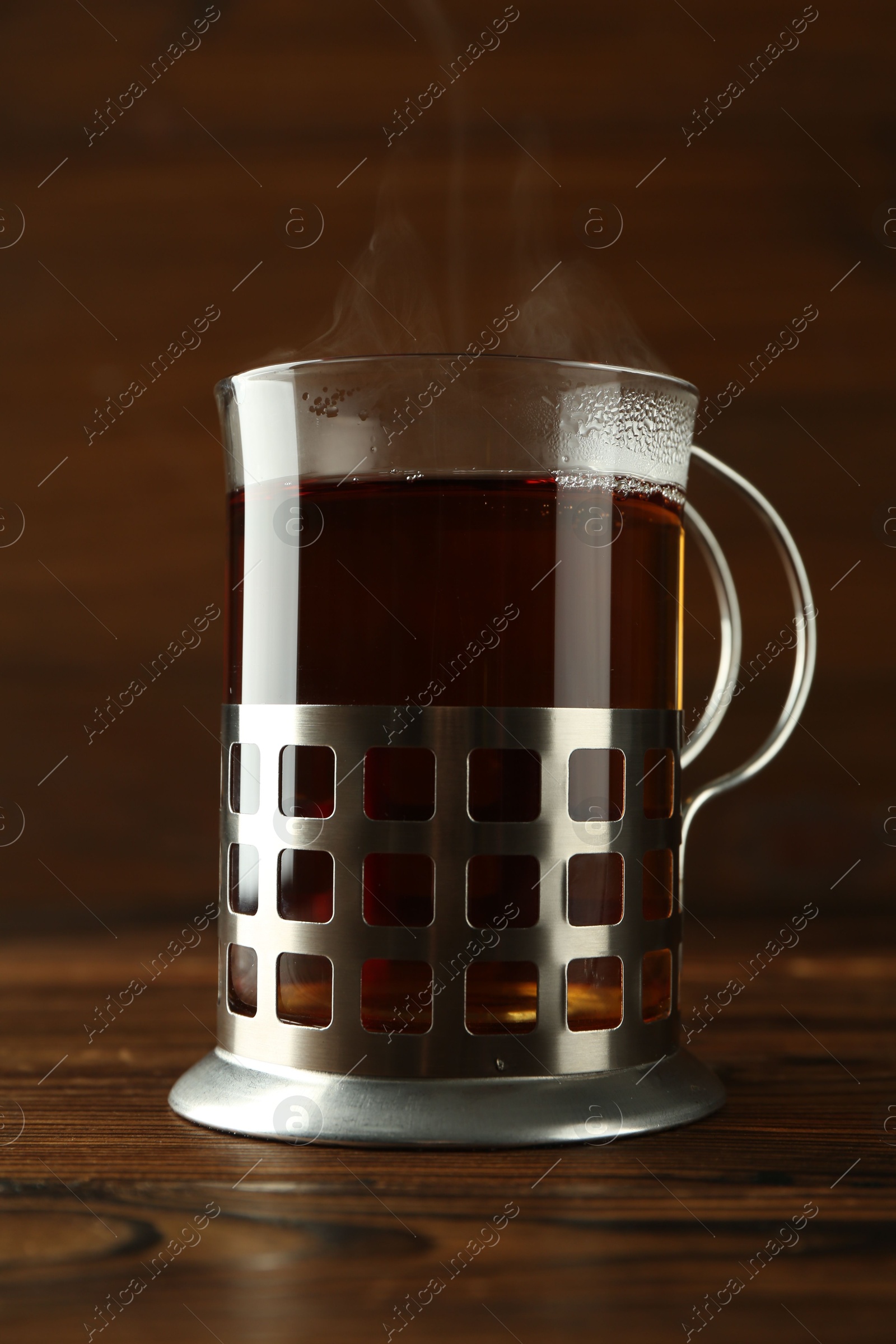 Photo of Glass of aromatic tea in holder on wooden table