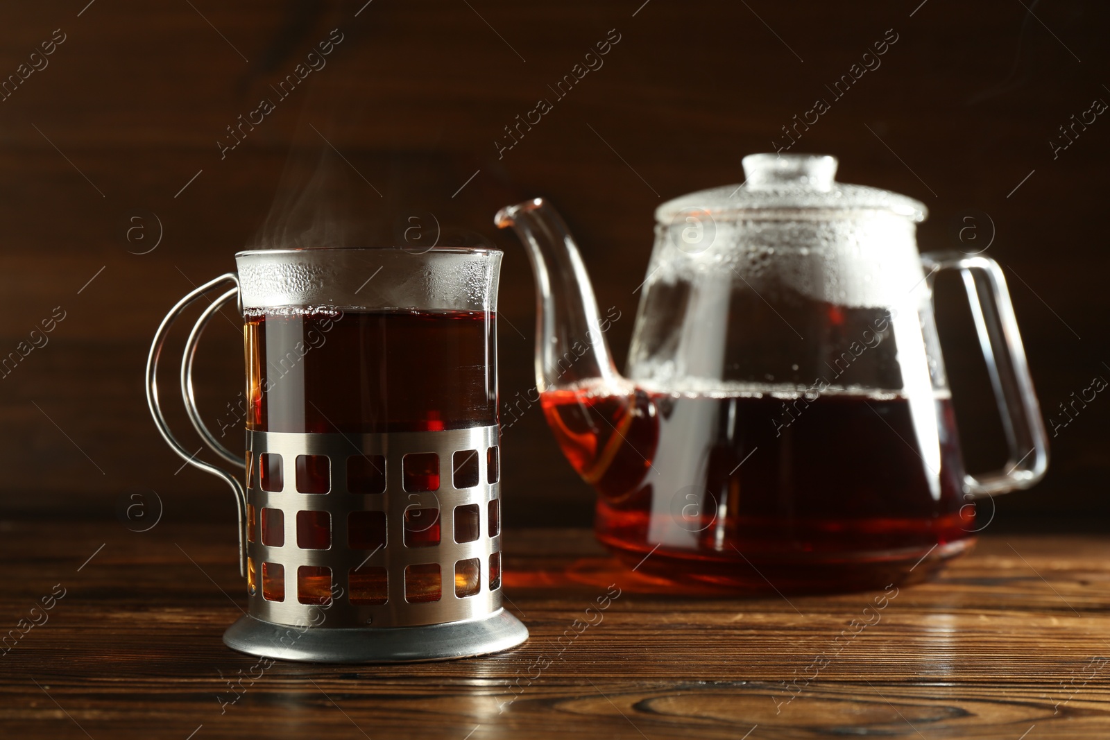 Photo of Glass of hot tea in holder and teapot on wooden table