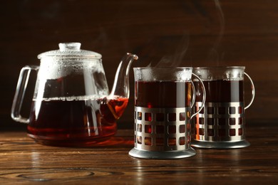 Glasses of hot tea in holders and teapot on wooden table