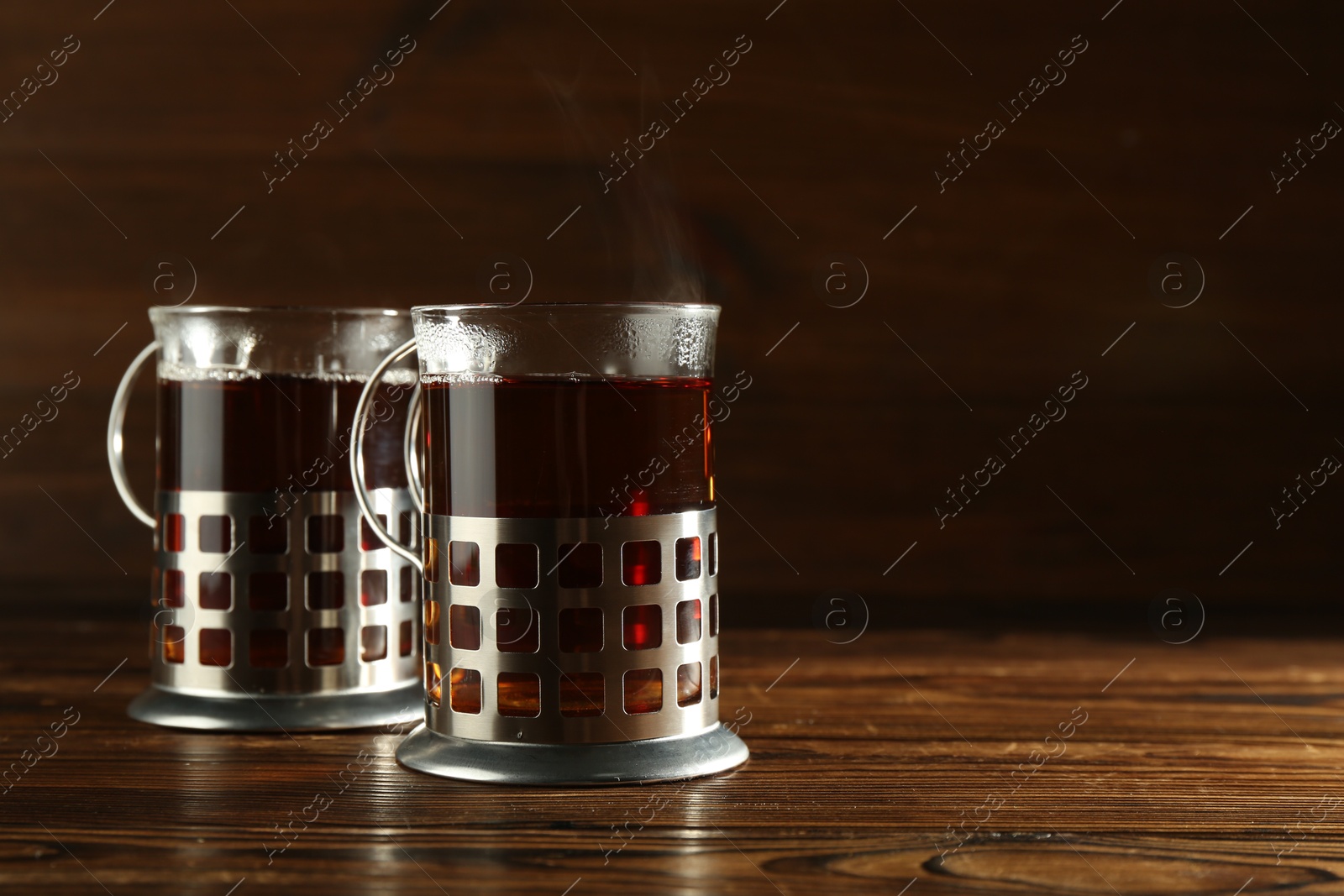 Photo of Glasses of hot tea in holders on wooden table, space for text