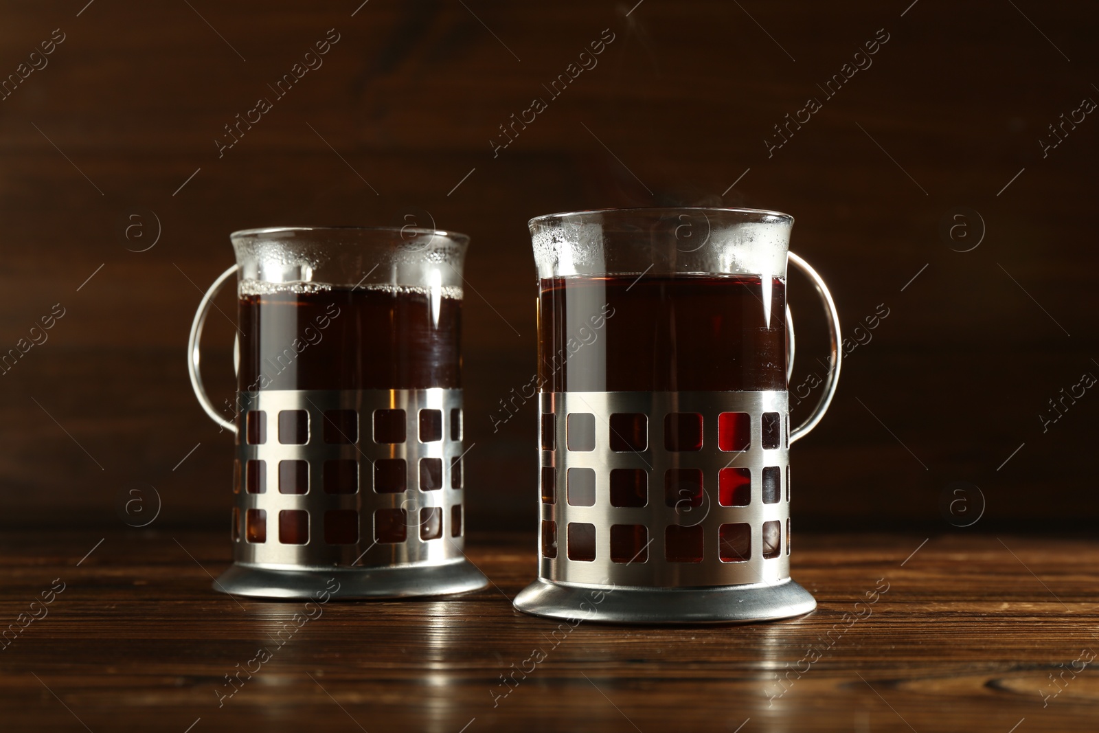 Photo of Glasses of hot tea in holders on wooden table