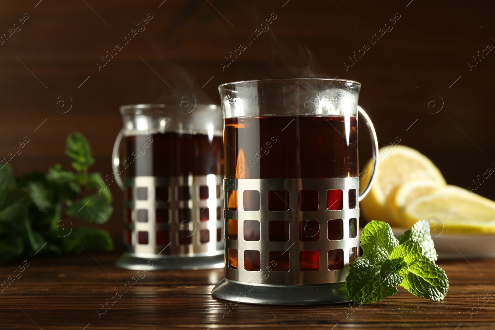 Photo of Glasses of hot tea in holders, mint and lemon on wooden table, closeup