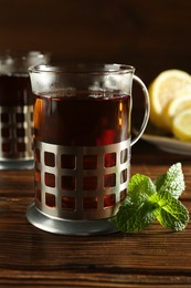 Photo of Glasses of hot tea in holders, mint and lemon on wooden table, closeup