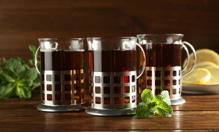 Photo of Glasses of hot tea in holders, mint and lemon on wooden table