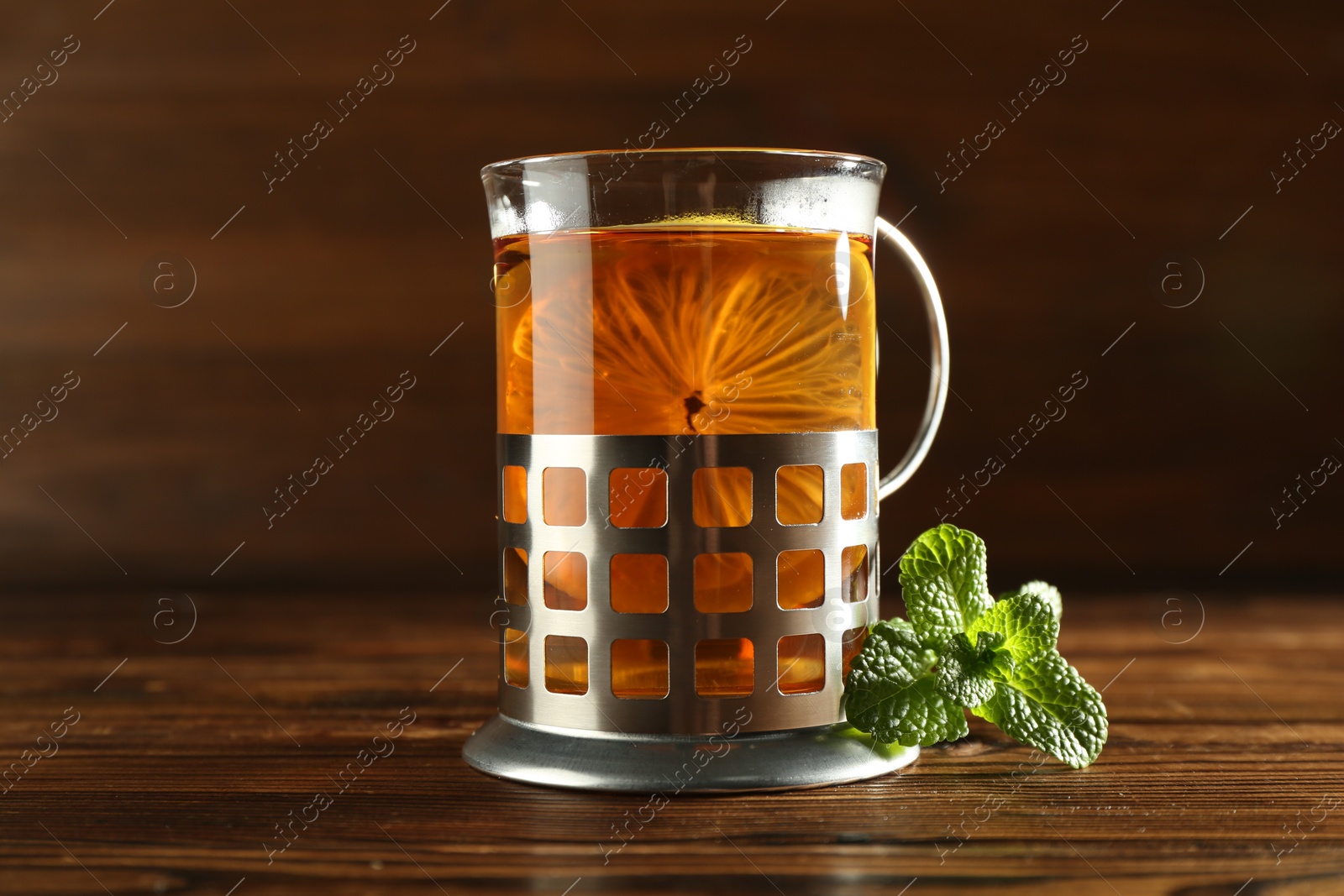 Photo of Glass of hot tea with lemon in holder and mint on wooden table, closeup