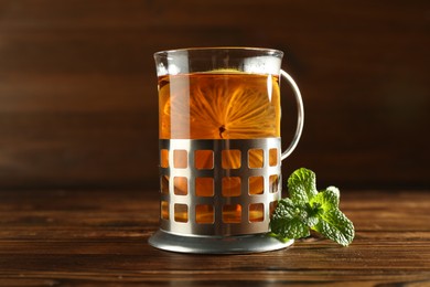 Glass of hot tea with lemon in holder and mint on wooden table, closeup