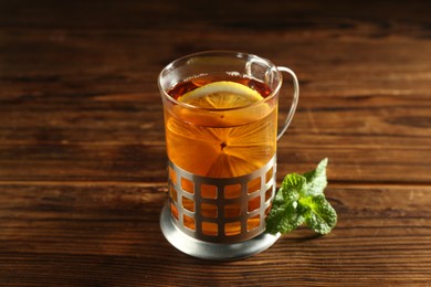 Glass of hot tea with lemon in holder and mint on wooden table, closeup