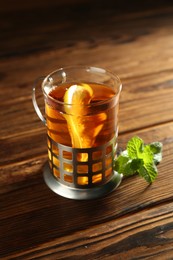 Photo of Glass of hot tea with lemon in holder and mint on wooden table