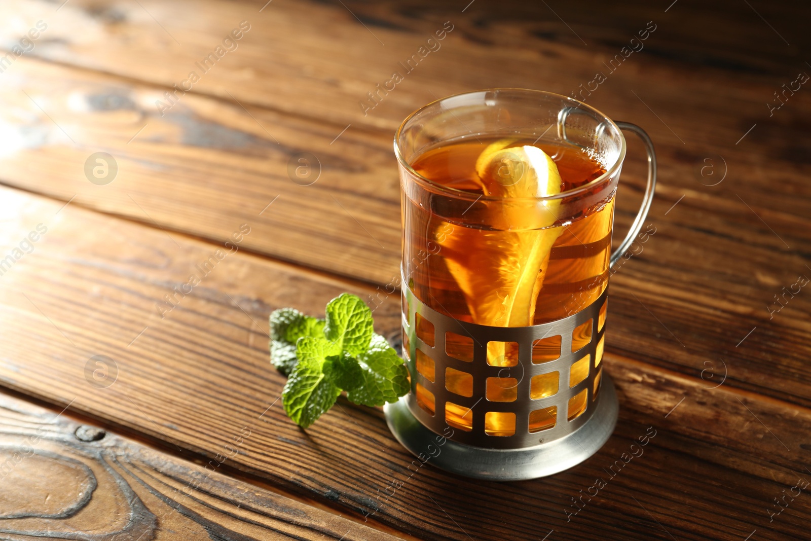 Photo of Glass of hot tea with lemon in holder and mint on wooden table, closeup. Space for text