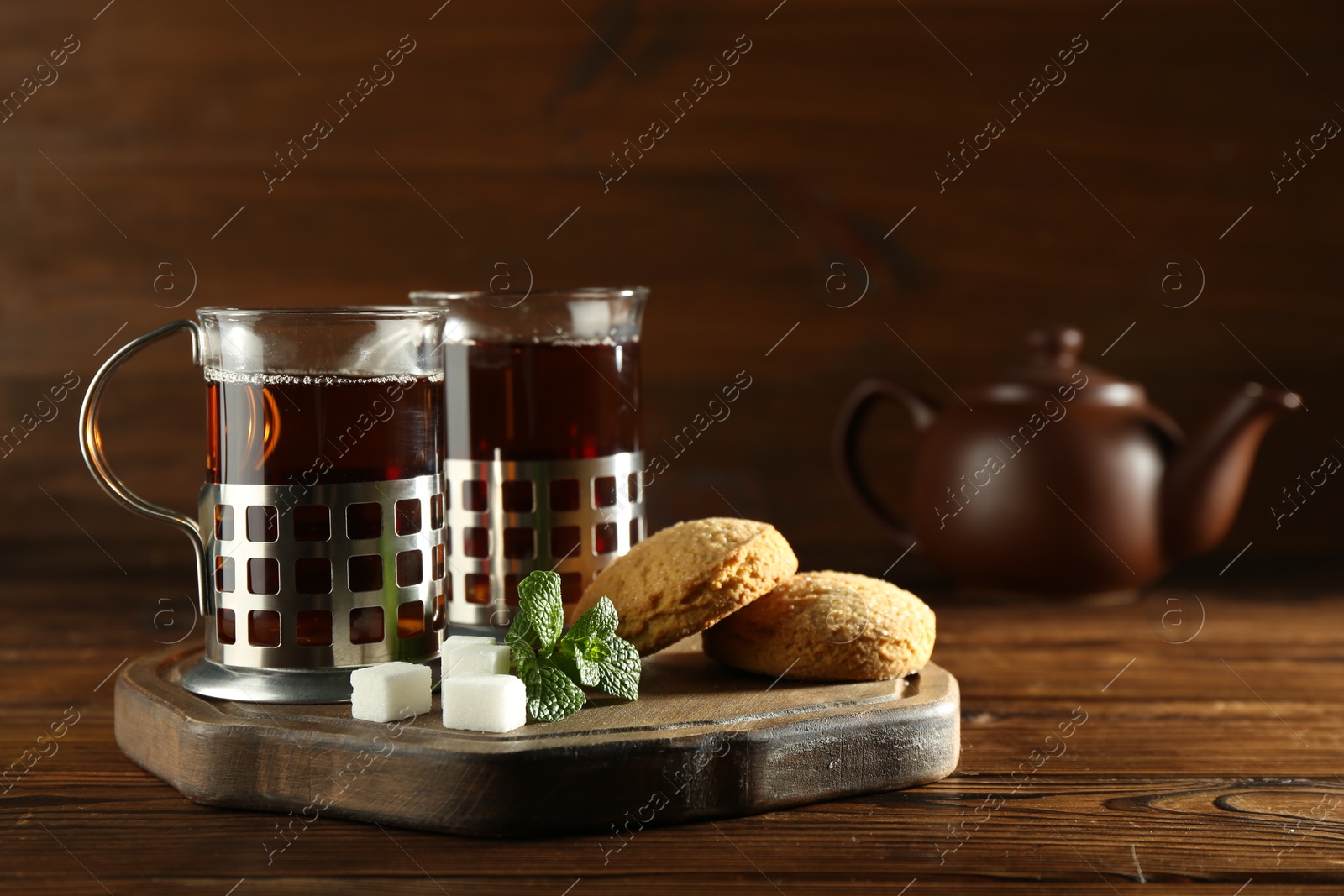 Photo of Glasses of hot tea in holders, sugar cubes and mint on wooden table, space for text