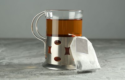 Hot drink in glass holder and tea bag on grey table