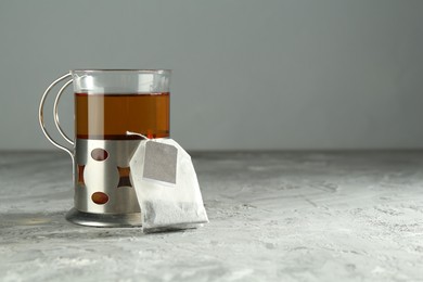 Hot drink in glass holder and tea bag on grey table, space for text