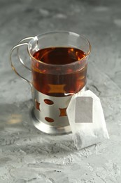 Hot drink in glass holder and tea bag on grey table