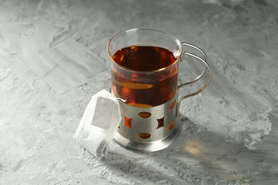 Photo of Hot drink in glass holder and tea bag on grey table