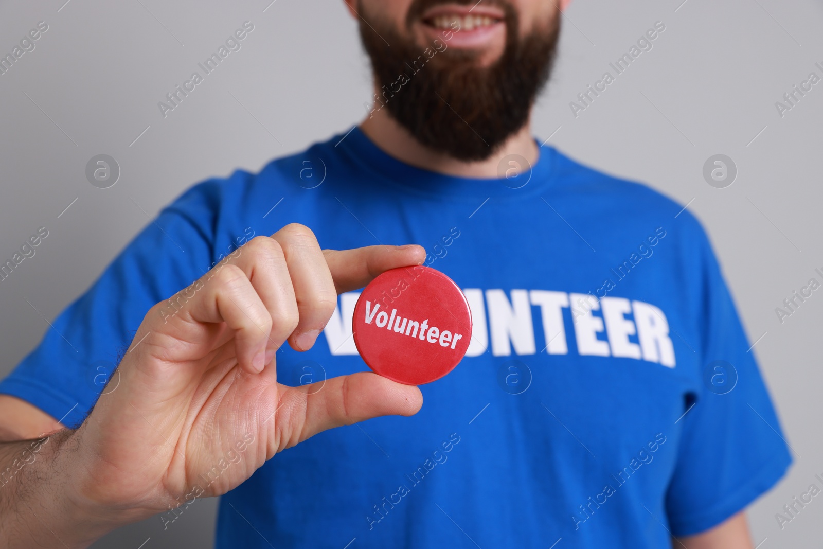 Photo of Man holding button badge with word Volunteer on light grey background, closeup