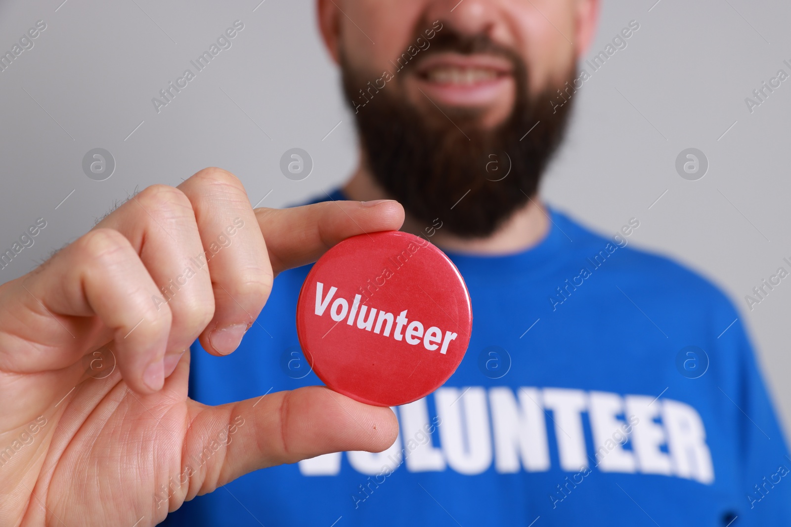 Photo of Man holding button badge with word Volunteer on light grey background, closeup