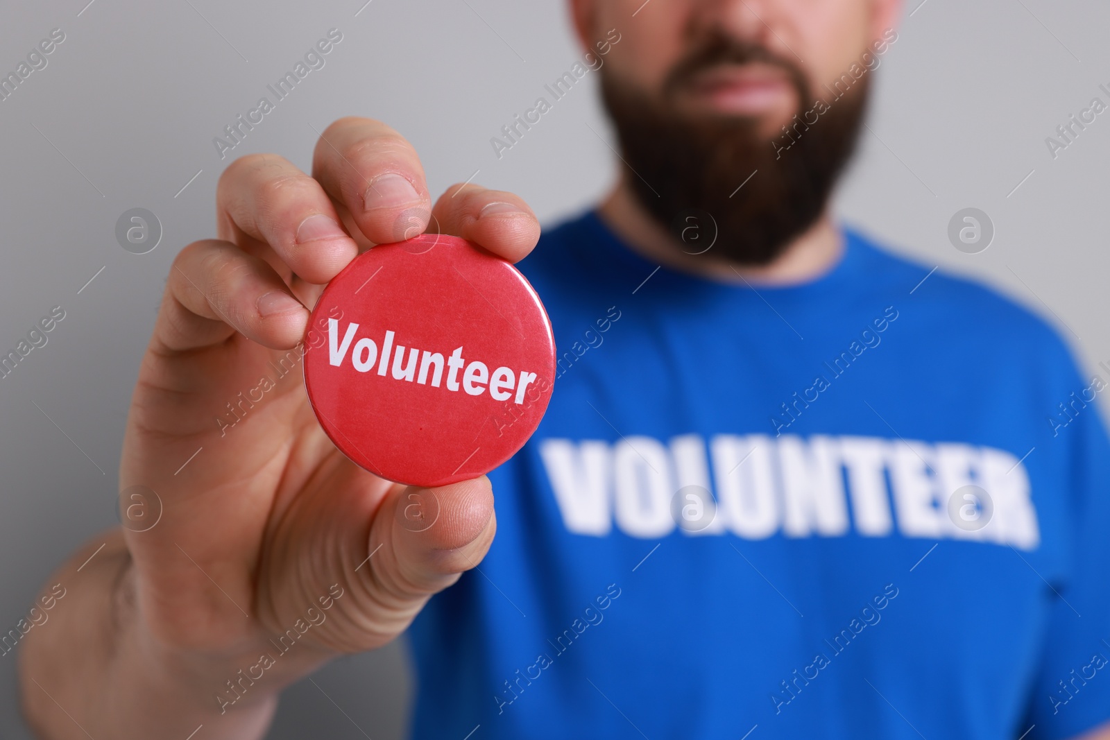 Photo of Man holding button badge with word Volunteer on light grey background, closeup