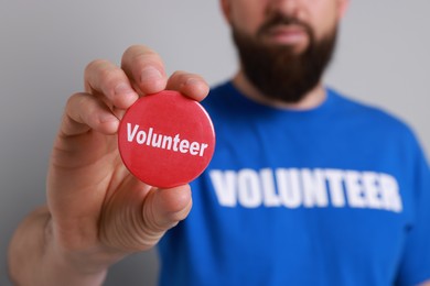 Photo of Man holding button badge with word Volunteer on light grey background, closeup