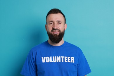 Positive man wearing t-shirt with word Volunteer on light blue background