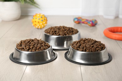 Photo of Dry pet food in feeding bowls and toys on floor indoors