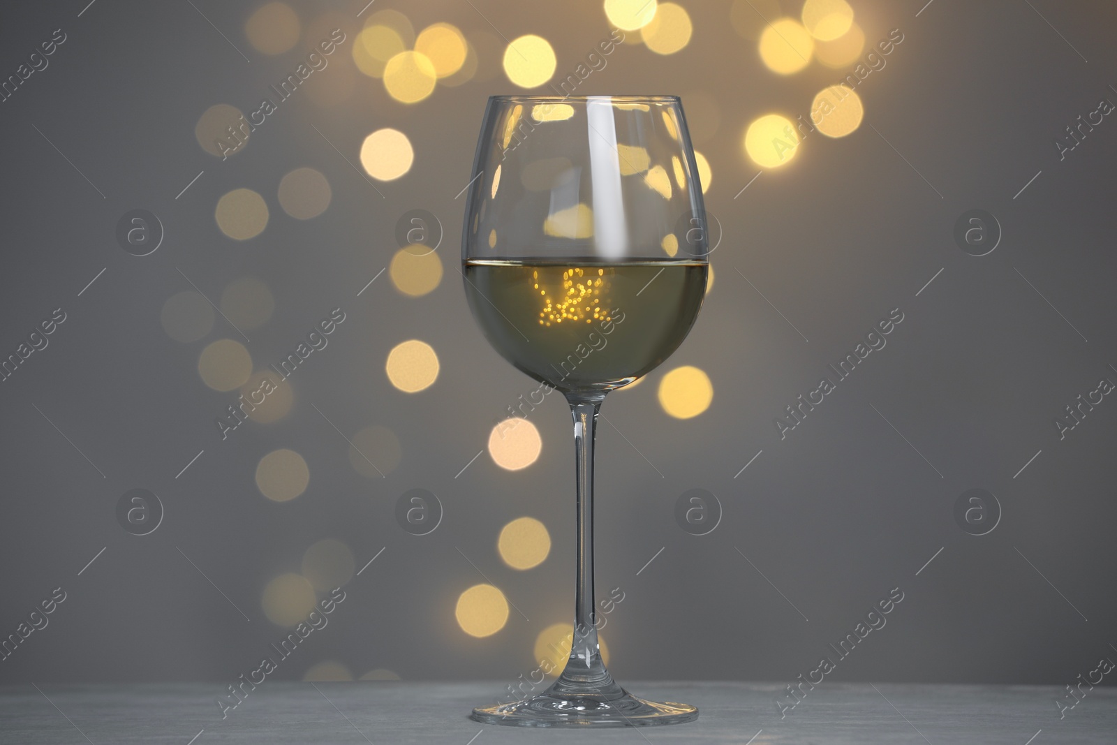 Photo of Tasty white wine in glass on table against grey background with blurred lights, bokeh effect